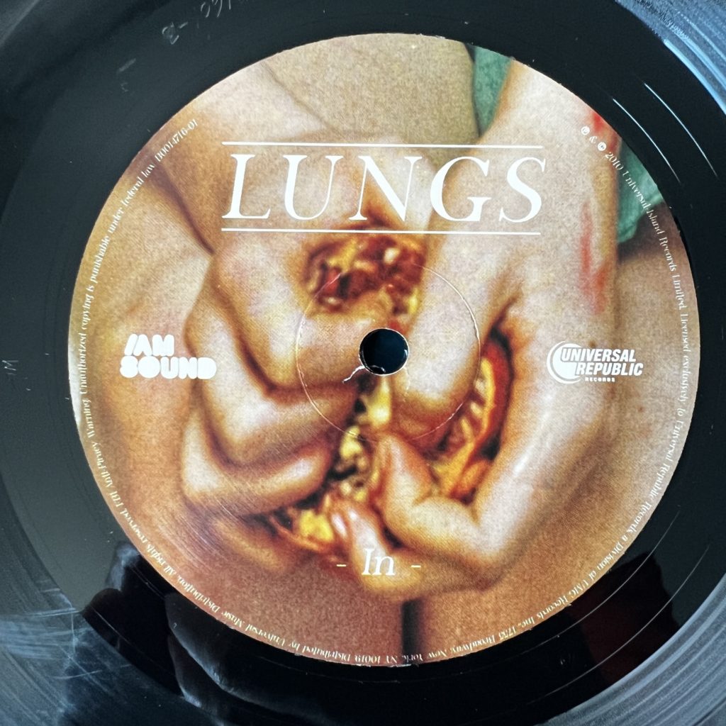Lungs A Side Label, marked "In", depicting hands tearing apart a seeded fruit.
