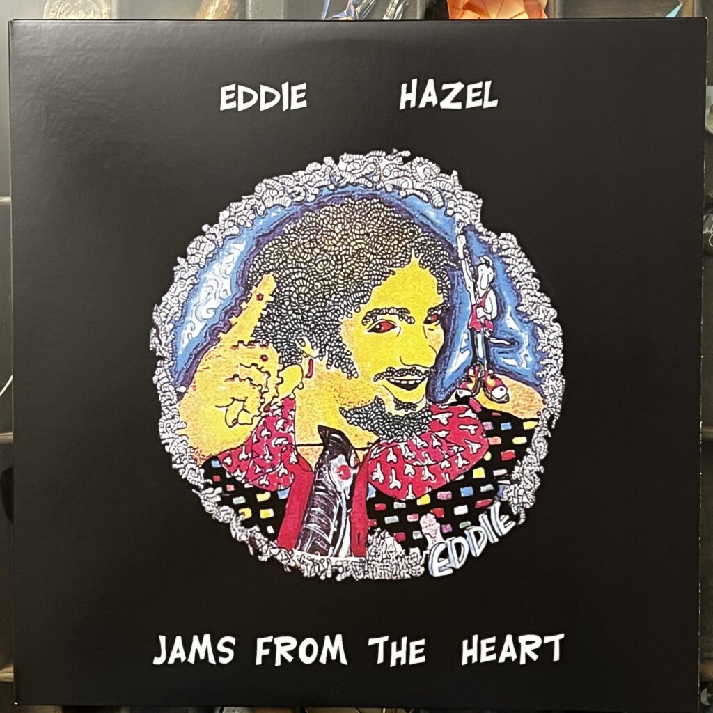 Eddie Hazel Jams From The Heart front cover – a black background with hand-drawn type for the title near the bottom. The illustration by Pedro Bell is a cartoony colored marker drawing of Eddie Hazel in a circle. The circle appears to be made up of worms (probably a reference to Maggot Brain), and Eddie's hair and beard have a similar look. his skin is yellow marker, his eyes red, his visible hand, pointing up to the sky, covered in little knobs or warts. His clothing is made up of a red collar with small designs over it, and a black covering with small colorful rectangles decorating it.  