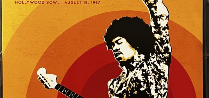 A black and white image of Jimi Hendrix, showing the upper half of his body facing to the left, his guitar gripped at the base of the neck with his right hand, his left hand a fist in the air. He is in some kind of colorfully patterned shirt, his hair in a natural afro style. The background is a series of four concentric color circles, like a sunsplash behind him.