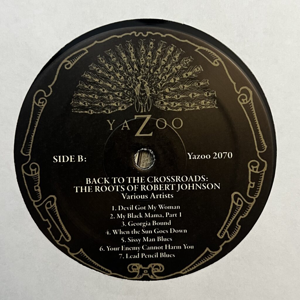 Yazoo records label for Back to the Crossroads. Around the label is art depicting curling, as if the label were curling at the edges. Above the label name is a drawing of a peacock.