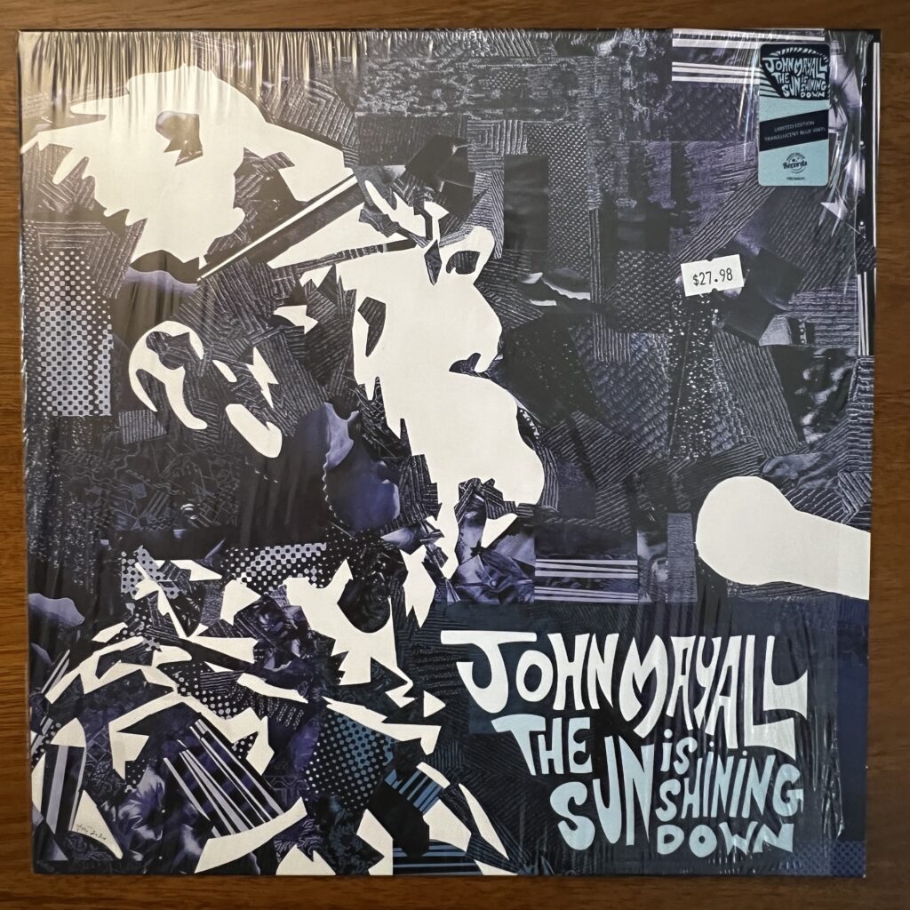 John Mayall The Sun Is Shining Down front cover – the cover is interesting stylized artwork made up of varying patterns, all in shades of blue, put together like quilt pieces to form an imagine of John Mayall (head and shoulders) in profile, wearing glasses, leaning his head back and singing with a microphone before him.