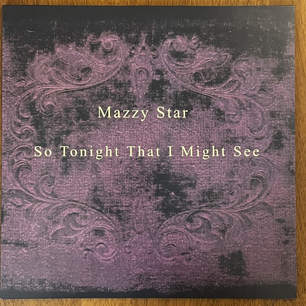 The front cover of Mazzy Star's "So Tonight That I Might See." The cover is simply the title in a very simple Times New Roman style font, overlaid on a decorative scrollwork that looks to be from the Victorian era.